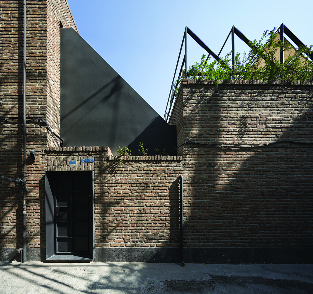 The alley entrance to Villa Nia, a narrow passage between brick walls with the rooftop garden structure visible above