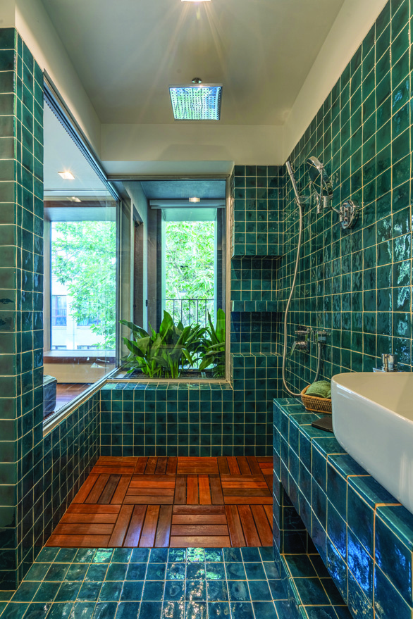Bathroom clad in deep green handmade ceramic tiles with warm wood plank flooring, a rain shower, and a window opening to lush garden greenery
