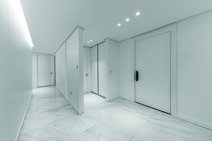 White marble corridor with minimalist design, recessed ceiling lighting, and apartment entry doors