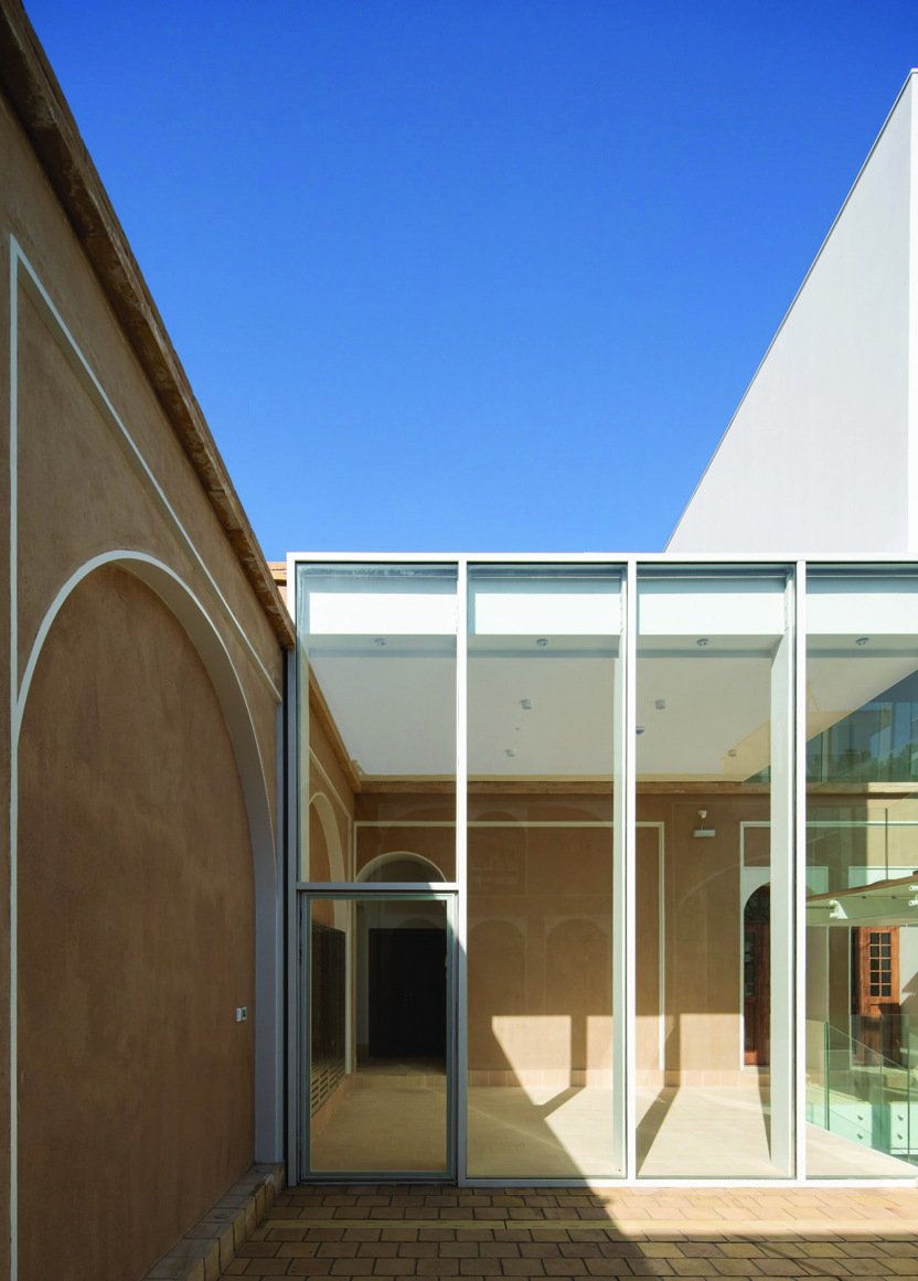 Detail of the glass wall meeting the restored clay-plastered wall with its arched niche, showing the junction between new and old materials