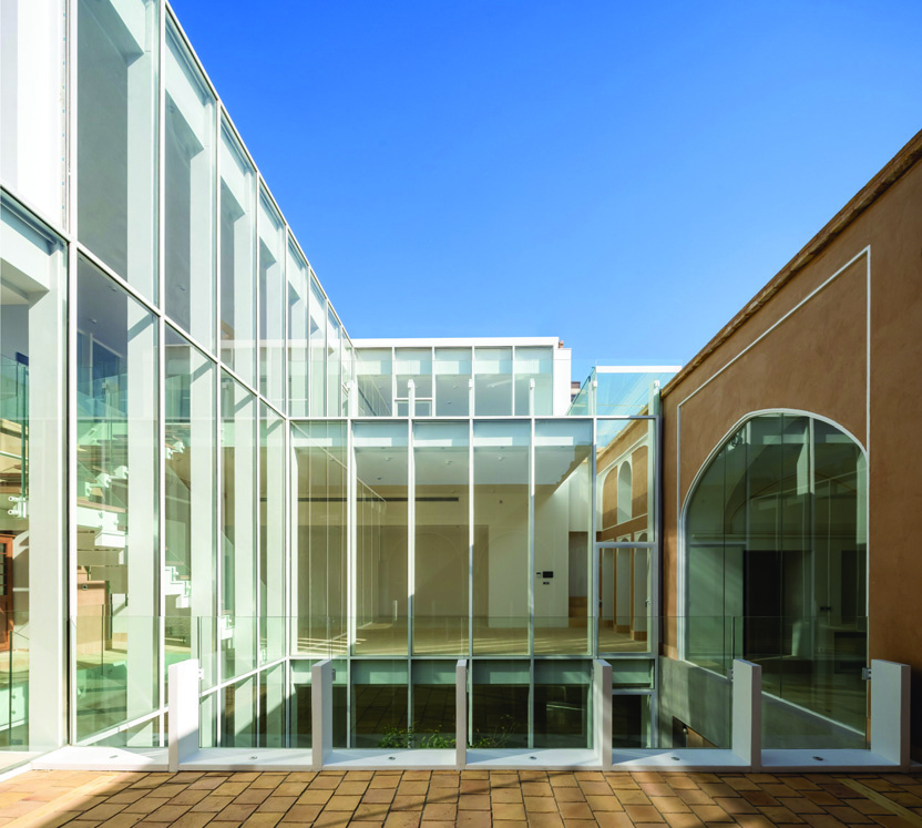 Daytime view of the courtyard with the full-height glass wall, restored arch, and reflecting pool below