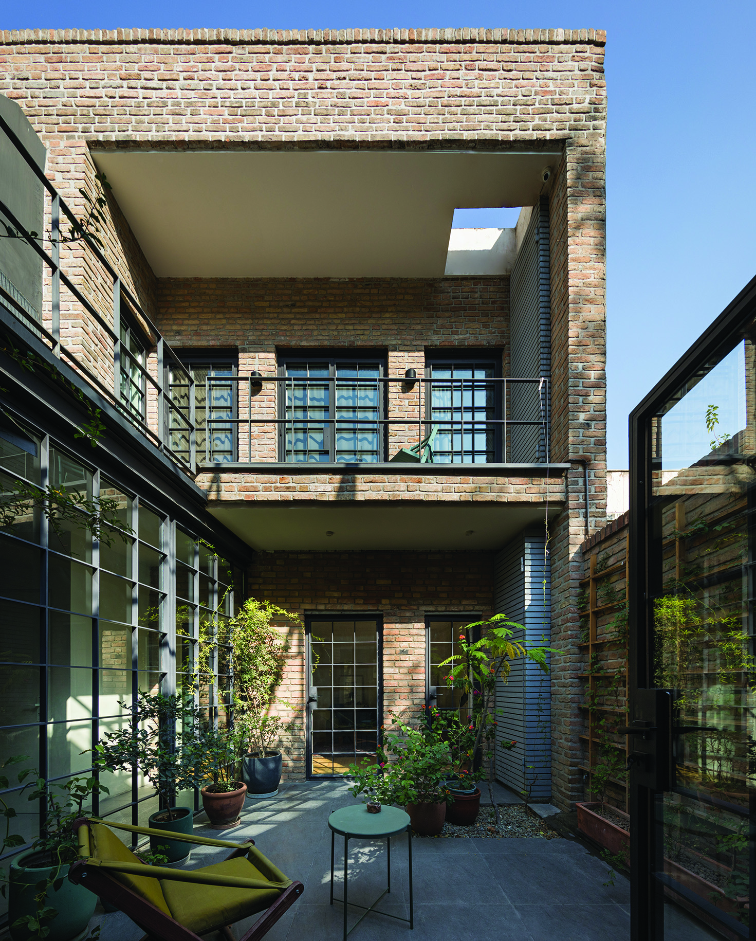 The central courtyard of Villa Nia showing two levels with brick walls, industrial steel-framed windows, lush plants, and lounge seating