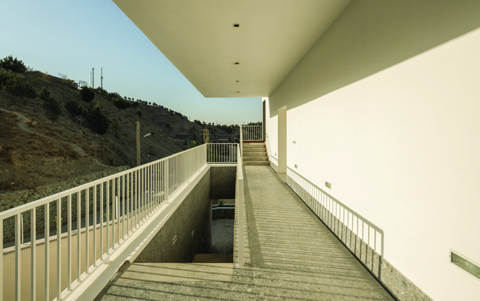 View under the covered walkway with parking level visible below and the staircase rising above against the mountainous landscape