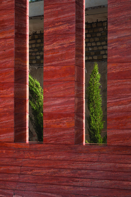 Close-up of two openings in the red stone wall showing cypress trees growing behind, the natural grain of the red Azarshahr stone clearly visible