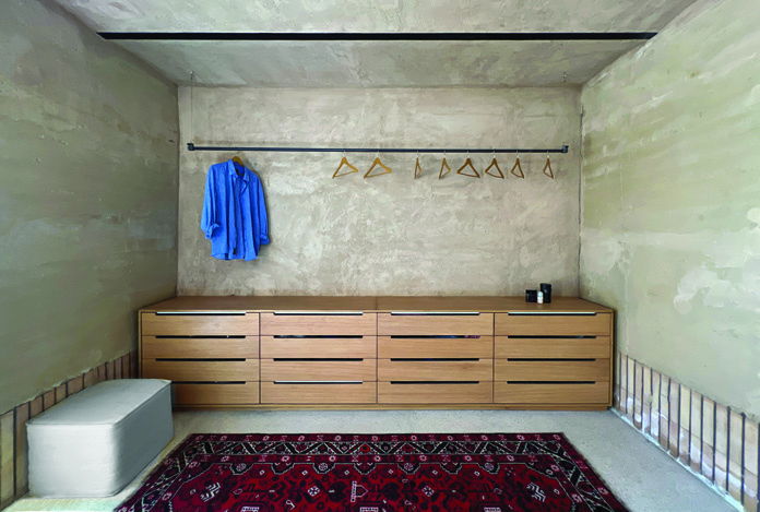 Dressing room with wooden drawer cabinet, clothing rack, rammed earth walls, and a traditional rug on the floor