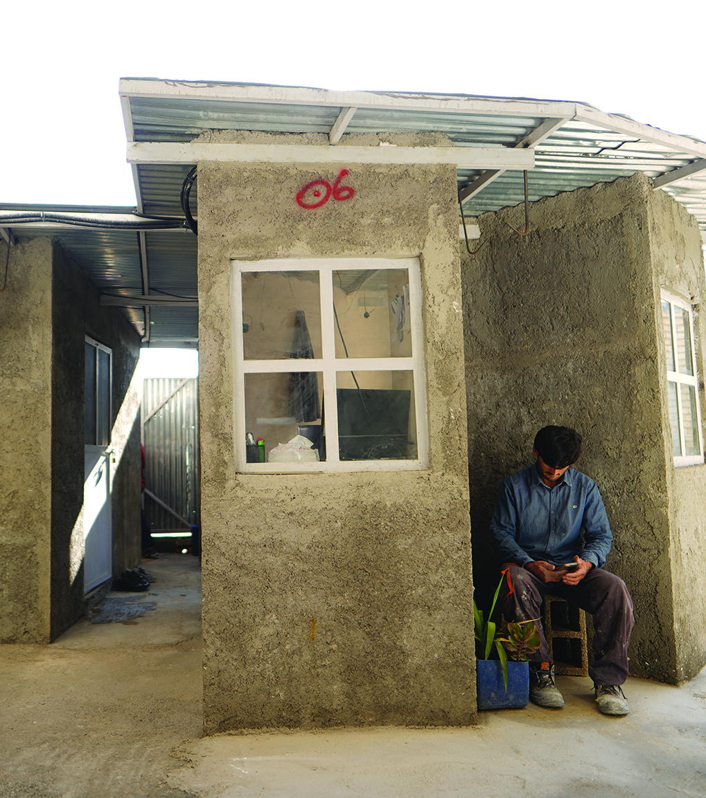 A worker sitting outside the horseshoe-shaped guardroom, with its curved brick wall and corrugated roof, fire extinguisher on the wall