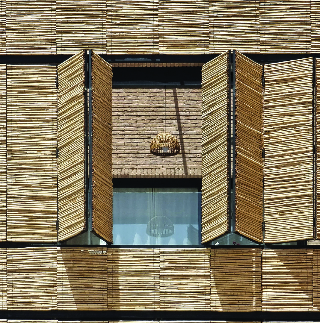 Close-up of the facade showing reed panels partially open, revealing a wicker pendant lamp and the brick interior of the balcony