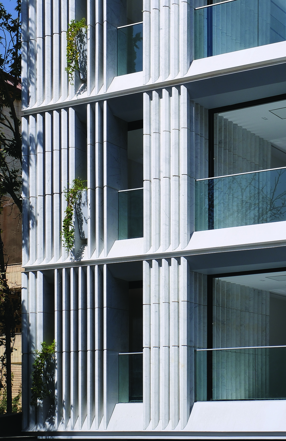 Detail of the stone fins and glass windows on the Sayeh Building facade, showing greenery growing between the vertical louvers
