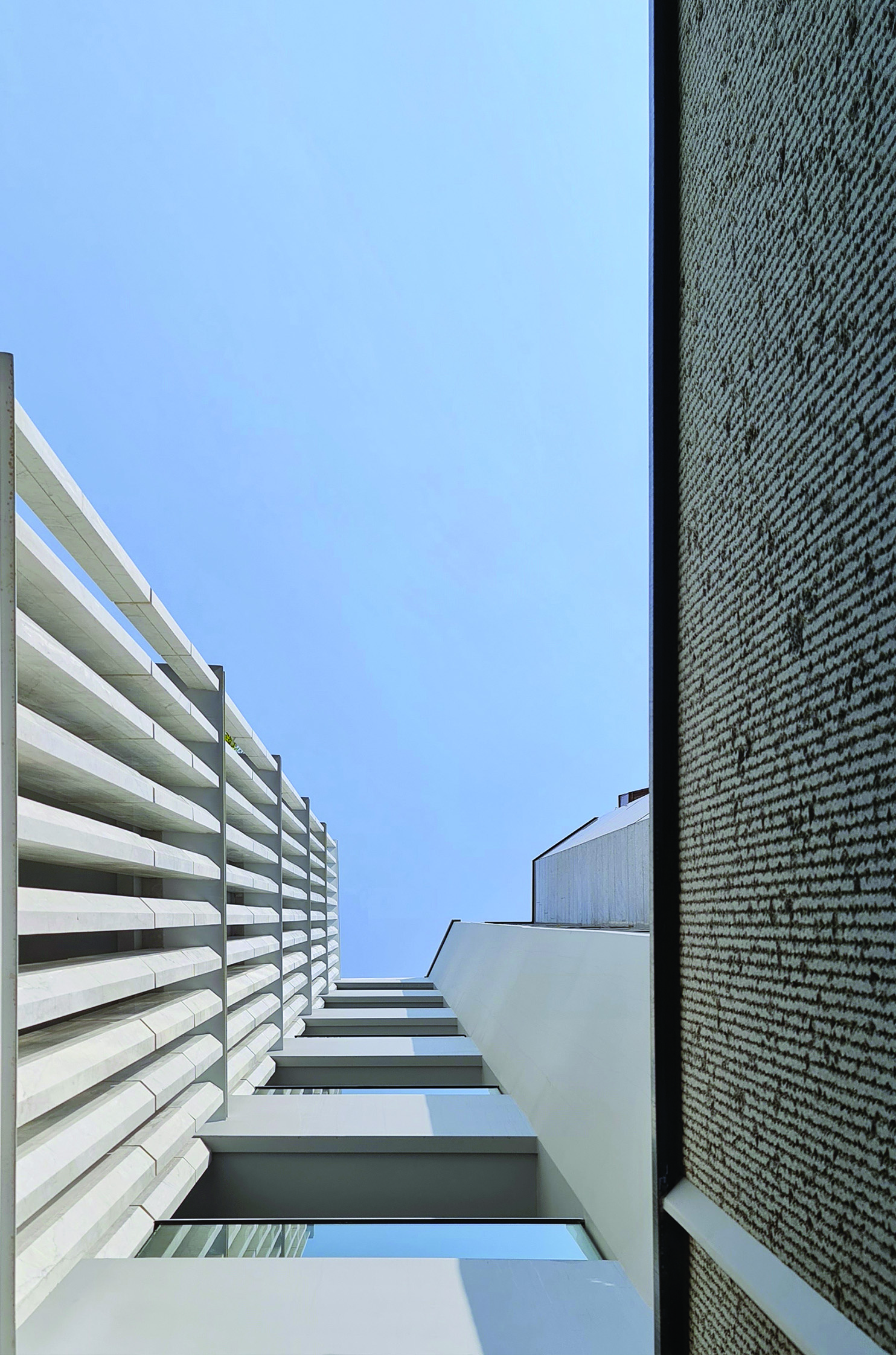 Looking upward between the Sayeh Building and its neighbor, the vertical stone louvers receding into the sky against a brick wall