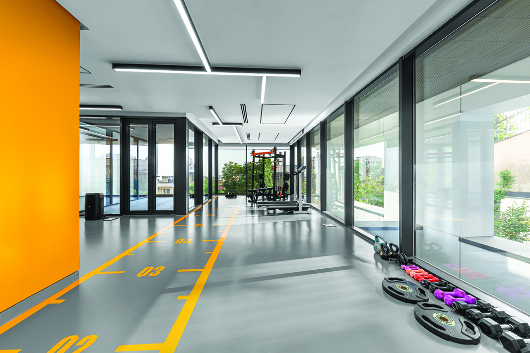 Modern fitness center with glass walls, grey floor with yellow sport markings, and exercise equipment