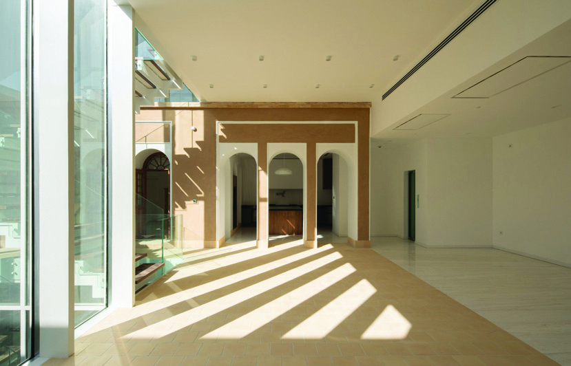 Interior view showing sunlight streaming through the glass wall onto the restored clay-plastered arches and stone floor
