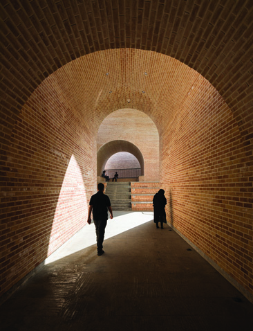 Interior brick vault corridor with dramatic light entering through a side opening, silhouettes of two pedestrians walking through the passage