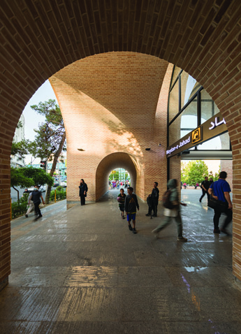 View through a brick arch passage looking toward the metro entrance sign and the city beyond, with pedestrians in motion