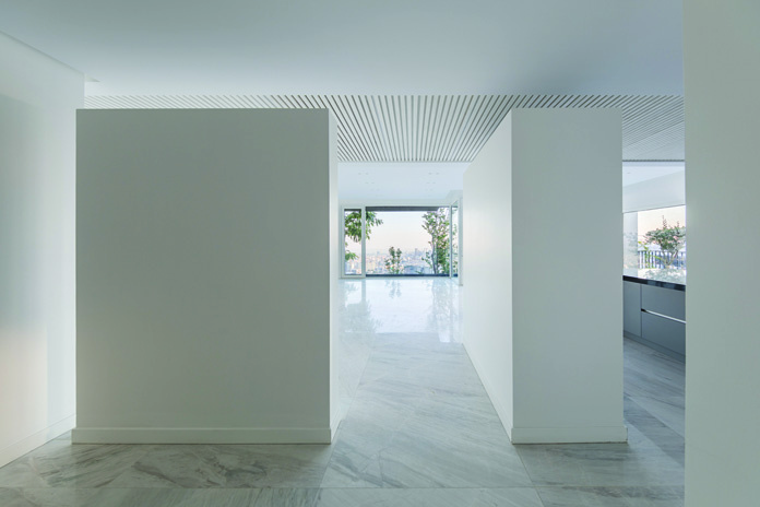 Interior view through white partitions toward a balcony window with trees visible outside and the city beyond