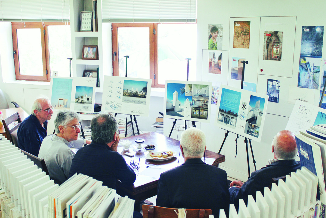 The five jury members seated around a table reviewing project submissions displayed on boards and easels