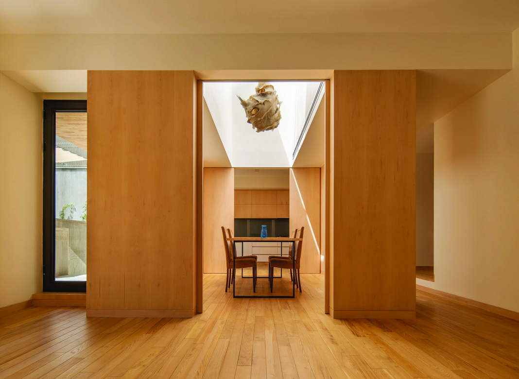 Interior view from the living room through to the dining area, with an overhead skylight flooding the wood-paneled space with natural light and an organic pendant lamp