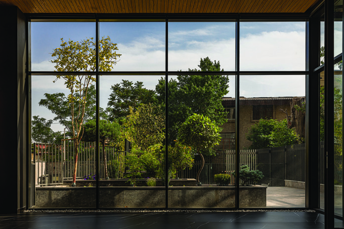 View through the lobby's full-height windows looking out onto the communal garden with mature trees and planting beds