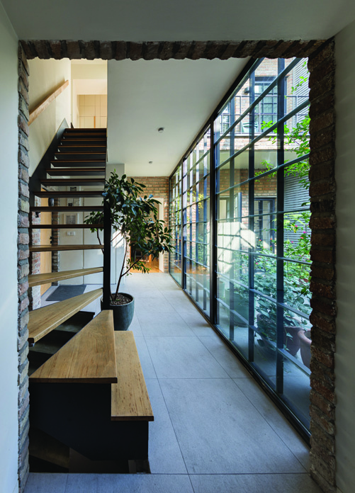 The entry lobby of Villa Nia with a floating steel and wood staircase, full-height glass wall looking onto the courtyard, and a ficus plant