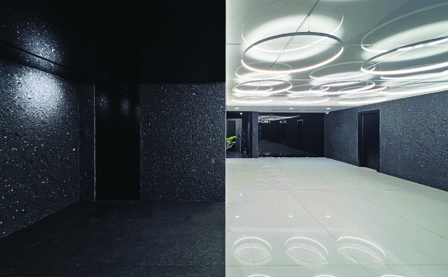 The building lobby split between dark terrazzo walls with dramatic lighting on the left and a bright white reception area with circular ring pendant lights on the right