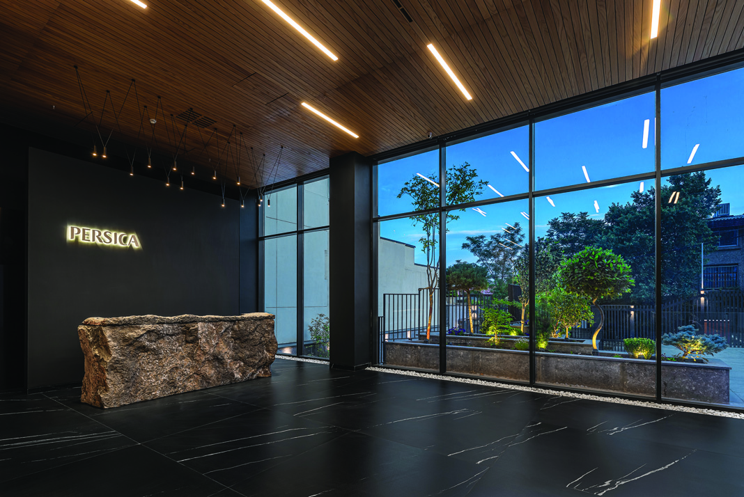 The lobby at twilight with the illuminated Persica sign and large windows looking out to the landscaped garden