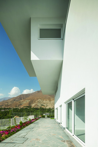Ground-floor terrace under the overhang of the upper volume, with a view of the garden and entrance