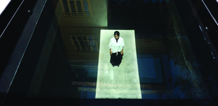 Overhead view through the glass courtyard floor at night, showing a person standing on the illuminated panel below