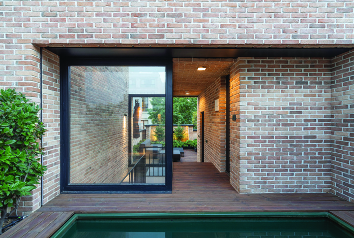 The rooftop pool area with a small green-tiled pool beside a wooden deck, a large glass sliding door revealing the interior, and brick walls surrounding