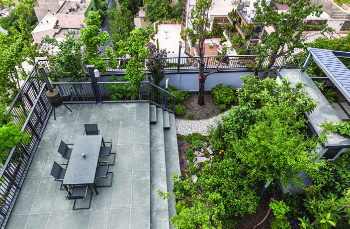 Rooftop terrace with a dining table set among trees, planters, and garden paths