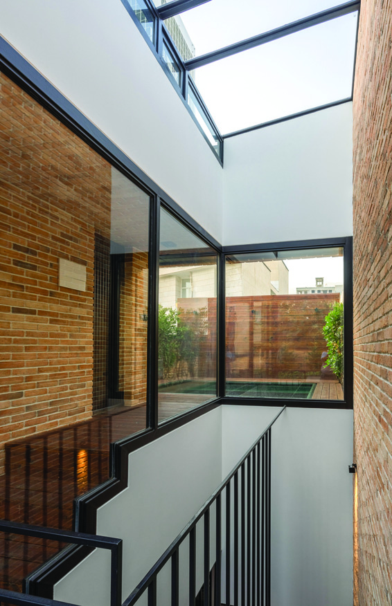Interior view of the stairwell with a glass ceiling skylight flooding light onto brick walls, metal railings, and a view through to the backyard garden