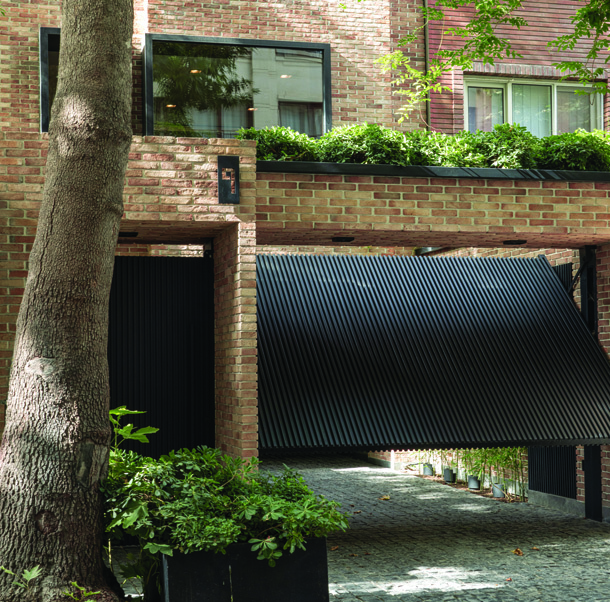 Street-level view of Hanna House showing the brick facade, metal parking gate, green planter above, and protruding window bays on upper floors