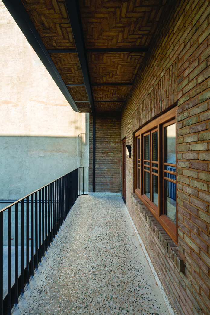 Covered terrace with herringbone-pattern brick ceiling, iron railing, terrazzo floor, and traditional wooden window with warm lighting