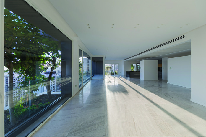 Interior of a residential unit with floor-to-ceiling windows looking onto the green planters, marble floors and minimal white walls