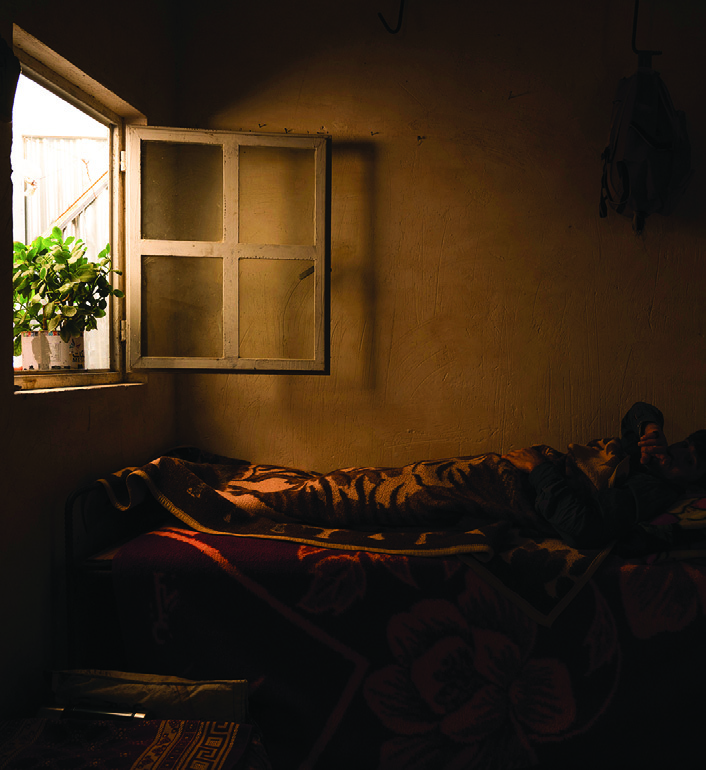 A worker resting on the bed in the bedroom area, with a small window letting in light from the gap between buildings