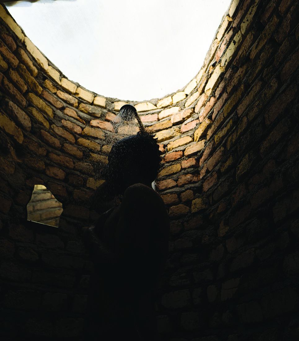 A worker showering in the curved brick bathroom, light streaming through the semi-transparent ceiling