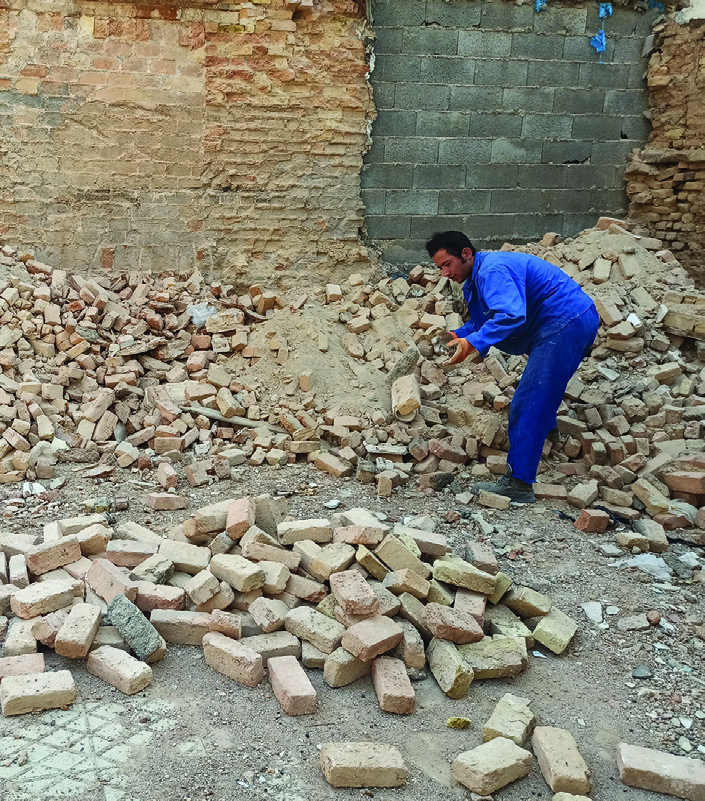 A worker sorting and stacking salvaged bricks for reuse in the construction of the temporary house
