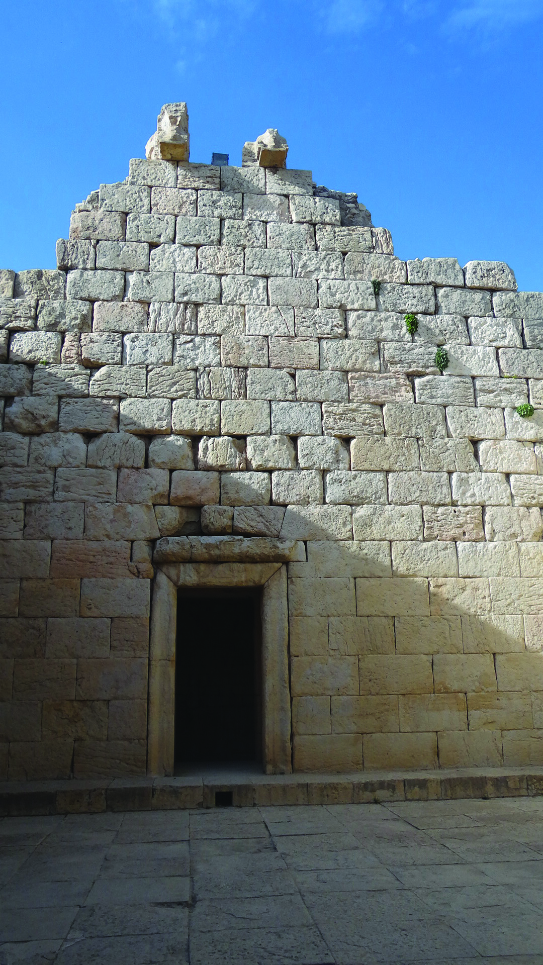 Stone wall facade of the Anahita temple at Bishapur with a doorway and remnants of bull sculptures atop the wall