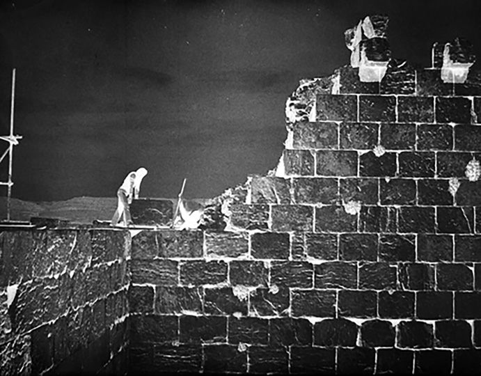 Detail of the massive stone wall of the Anahita temple with a worker for scale showing the enormous scale of the structure
