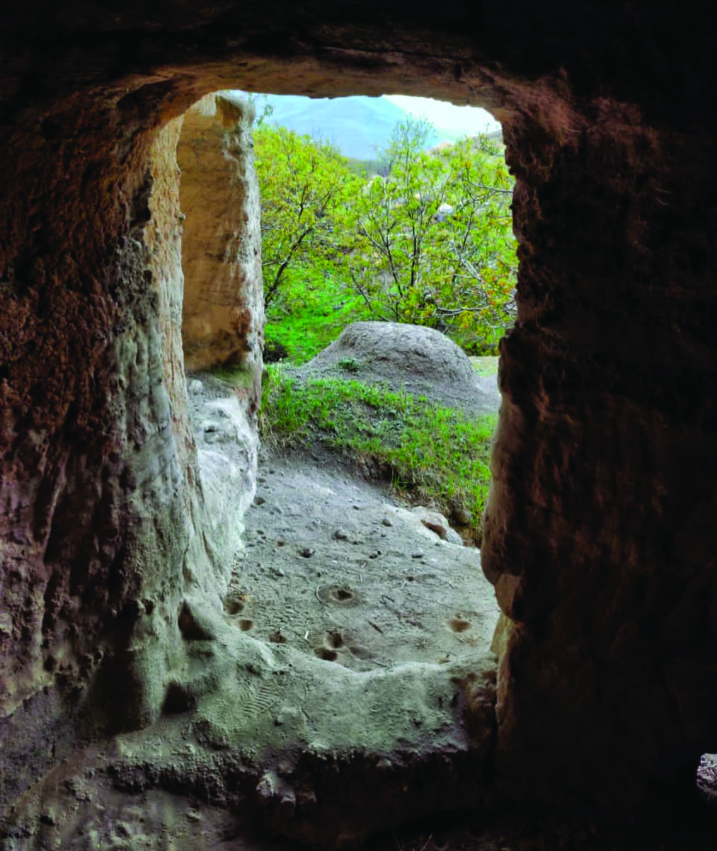View from inside a cave looking outward through a stone doorway, showing cup-mark hollows carved into the stone floor, at Jaraghil village near Mount Sabalan