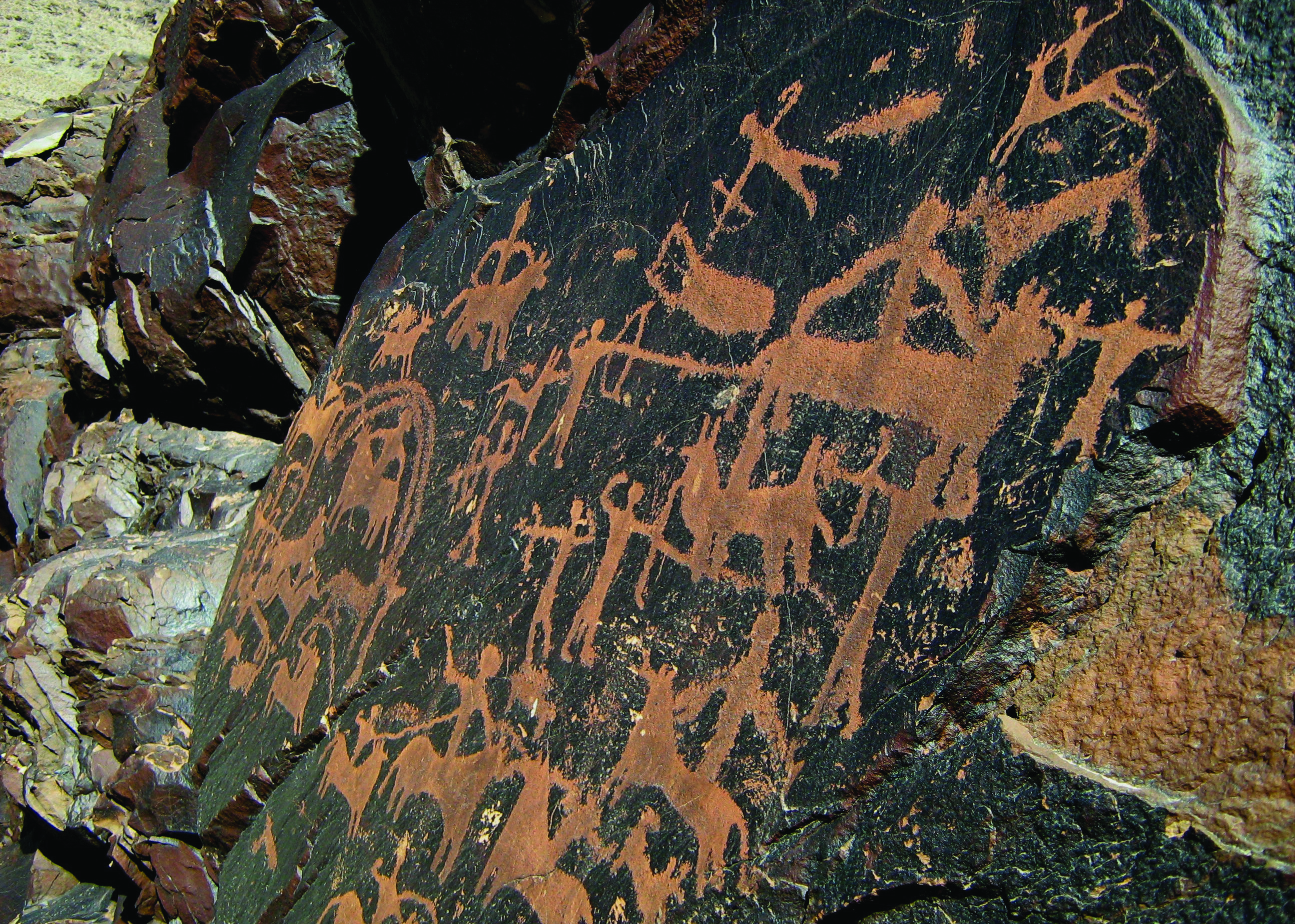 A large rock panel at Darreh Negaran covered with dozens of petroglyphs depicting hunters, horses, ibex, camels, and other figures in ochre tones