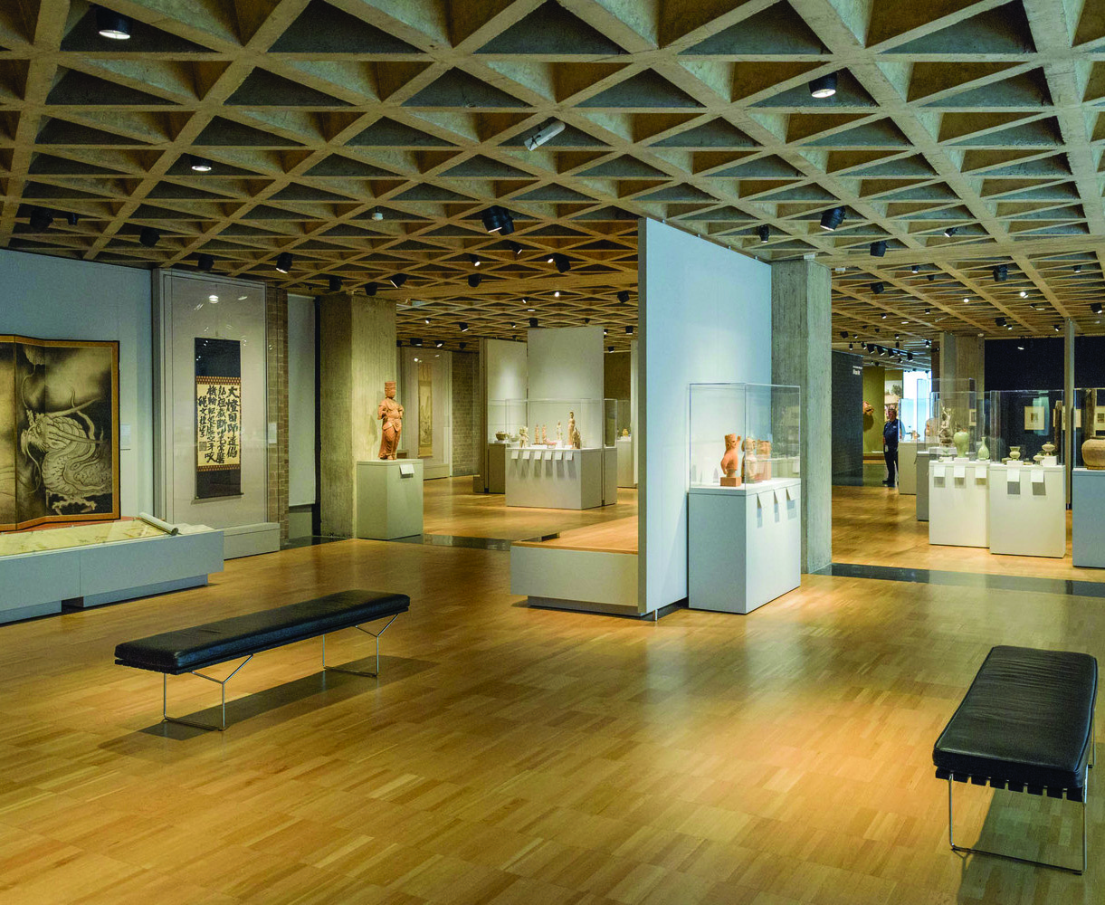 Color photograph of the Yale Art Gallery displaying Asian art beneath the tetrahedral concrete ceiling, showing sculptures and display cases