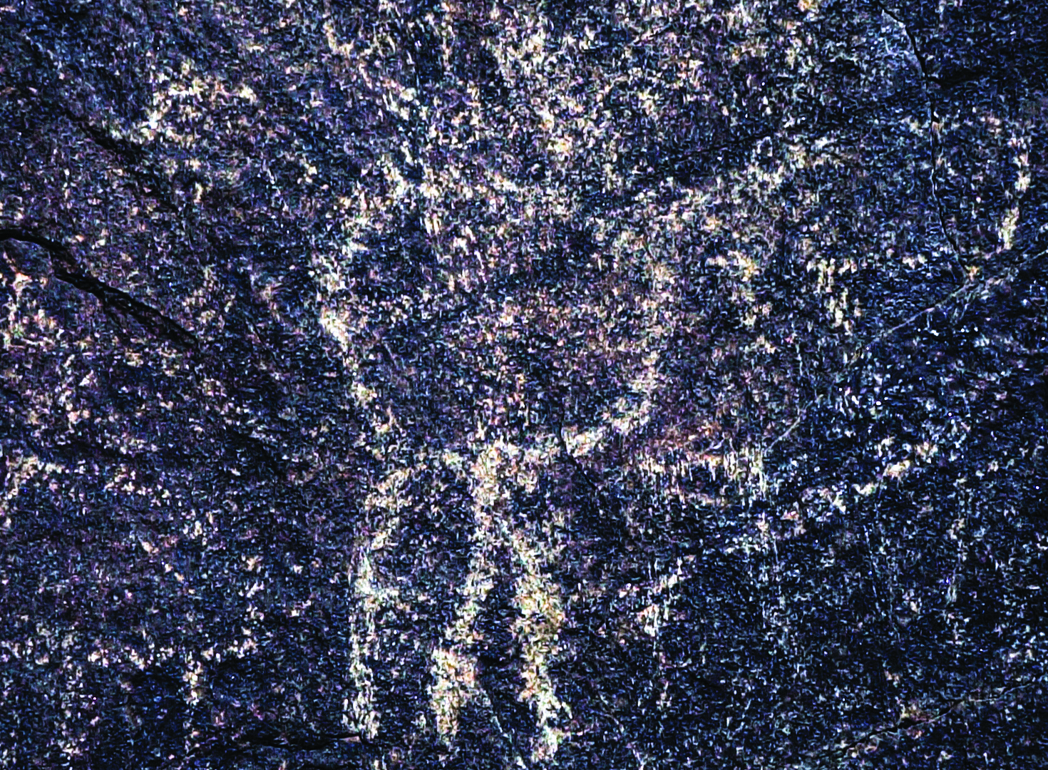 A faded human figure petroglyph on dark rock in the Hamedan region, barely visible due to weathering
