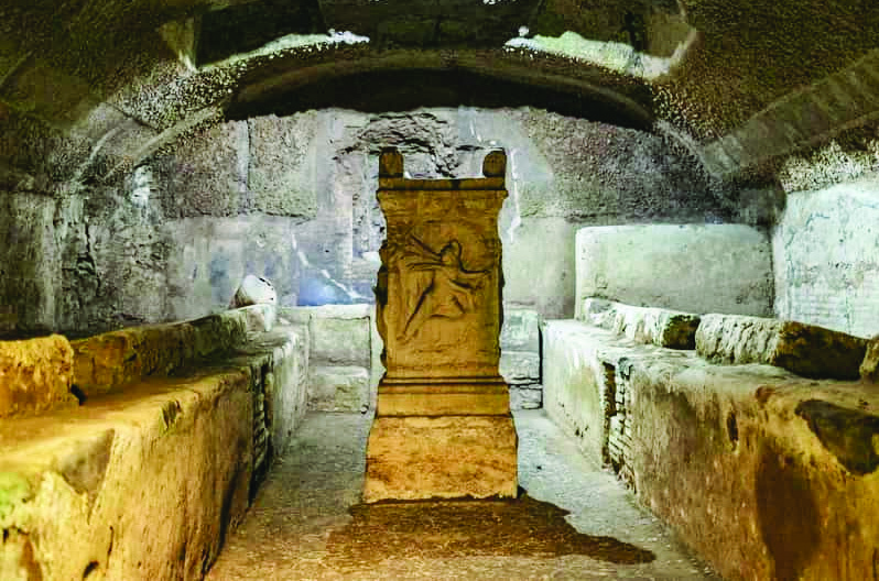 Underground Mithraeum beneath the Basilica of San Clemente in Rome, showing the vaulted chamber with stone benches along the walls and a central altar depicting Mitra slaying the bull