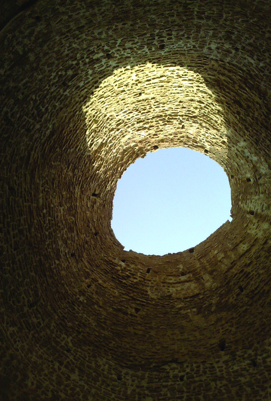 Looking upward through the stone dome of the Palace of Ardashir Babakan in Fars, Iran, with the circular oculus framing blue sky, surrounded by courses of ancient masonry