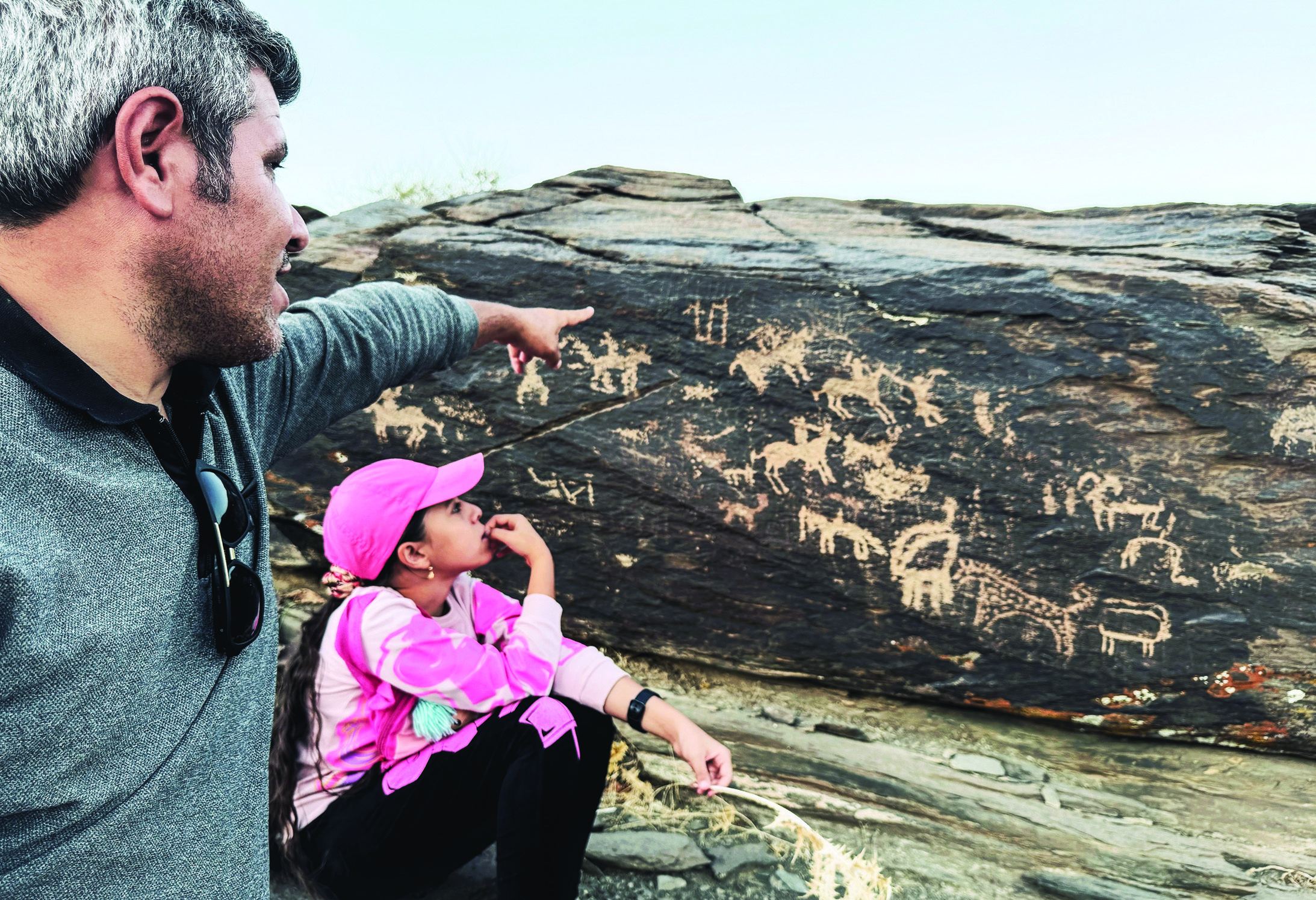 Rasoul Majidi and his young daughter pointing at petroglyphs on a large rock face at Teimareh