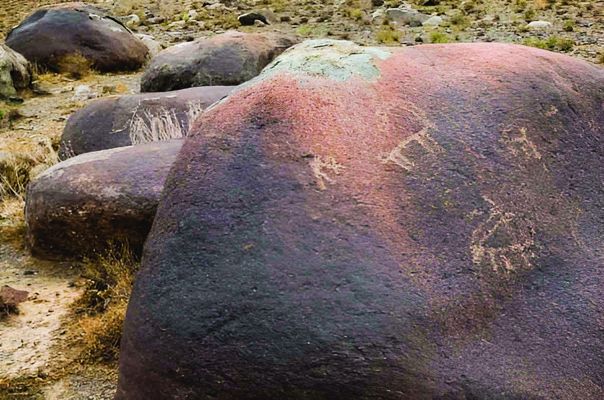 A large boulder on the Lathar Plain near Sialk bearing ancient petroglyphs of a goat figure carved into its reddish-purple surface, surrounded by arid rocky terrain