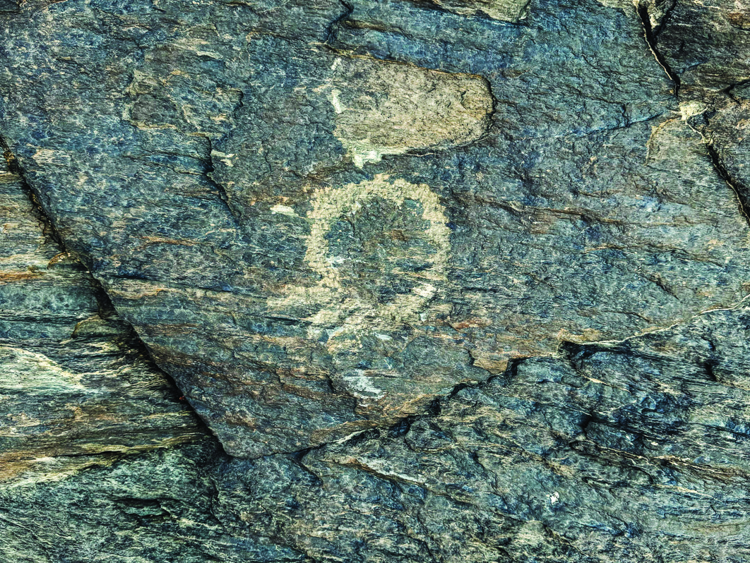 A circular sun-like symbol carved into rock at Teimareh, surrounded by weathered green-grey stone
