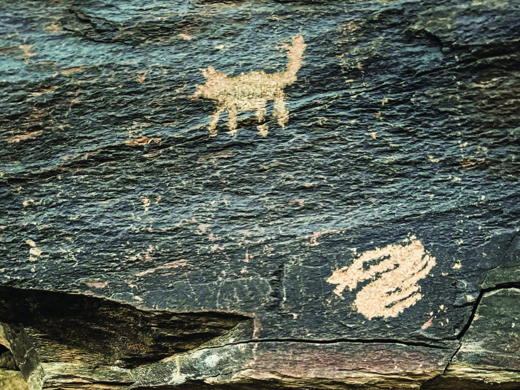 Teimareh petroglyph showing a feline figure and what appears to be a hand print or plant motif on dark rock