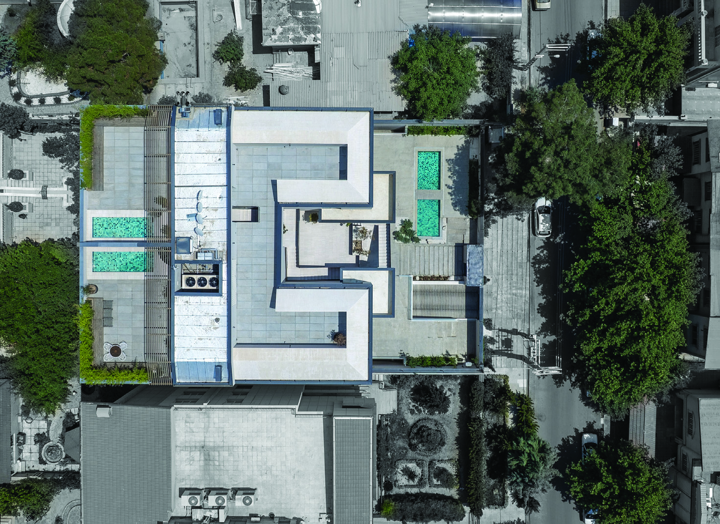 Aerial view of the Frenzy Stair building rooftop showing the stair void cutting through the centre, green planters on terraces, surrounding Karaj neighbourhood