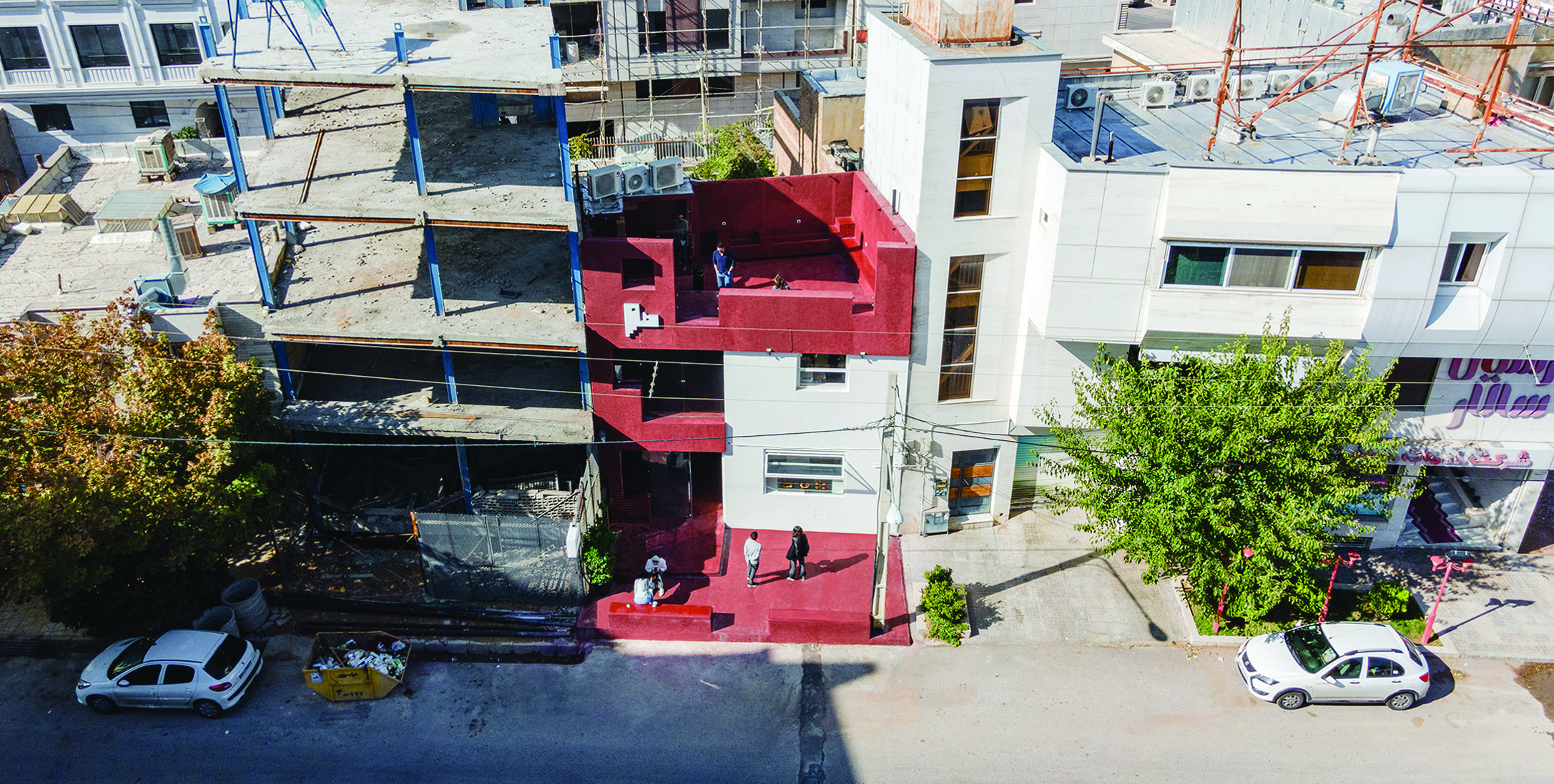 Elevated view of Journey Cafe from across the street, showing the red and white volumes in the context of neighbouring buildings and parked cars