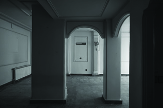 Before renovation: dark interior corridor of the original apartment with arched doorways and columns, dim lighting